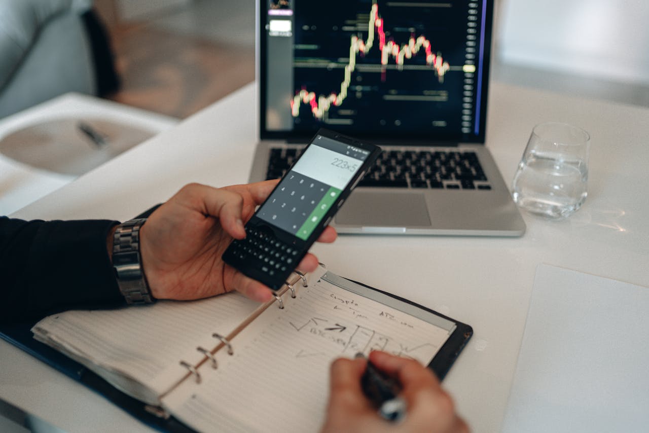 Close-up of a person using a calculator and laptop with stock charts for financial analysis.